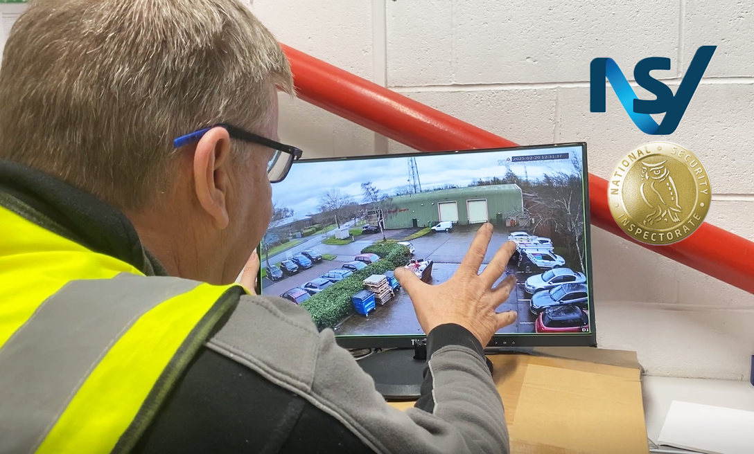 An engineer monitoring CCTV footage of a car park on a monitor and gesturing to the parked cars.