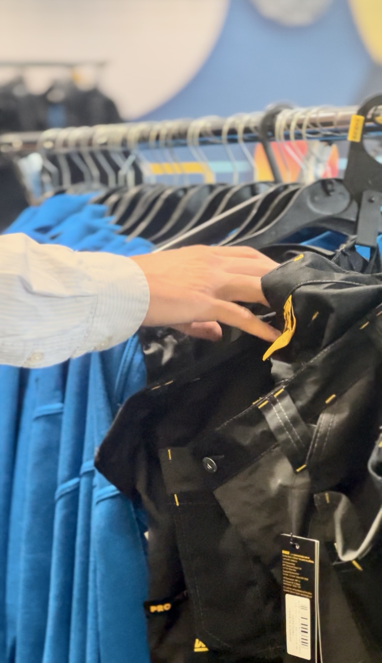 A hand grabbing a safety workwear jacket from a clothing rail