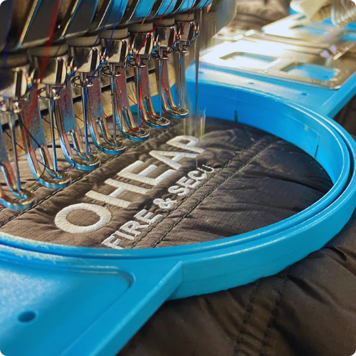 OHEAP-Embroidery-Services Embroidery machine stitching logo on flame-retardant jacket.