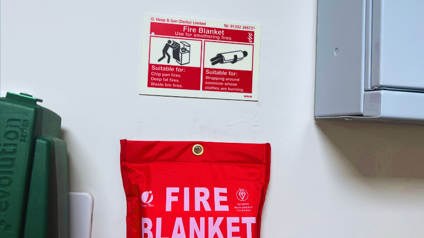 A kitchen fire blanket fitted to a wall below a fire safety sign