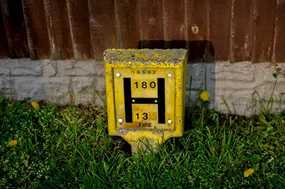 A yellow UK fire hydrant sign embedded in a grassy area